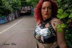 Mistress Elaina standing to camera in an urban environment, in leather underwear and chainmail.